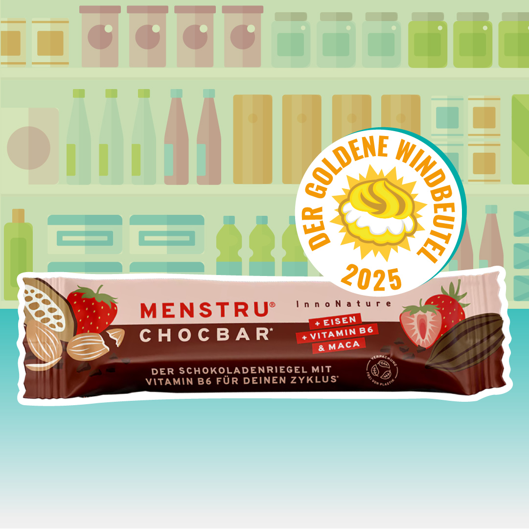 Quer liegende Verpackung des Schokoladenriegels „Menstru Chocbar“ (Erdbeere, Kakaobohne-Grafiken) vor Regal-Illustration; rechts oben das Siegel „Der Goldene Windbeutel 2025“.