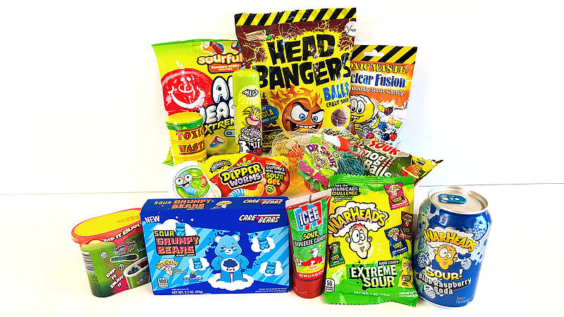 Verschiedene extrem saure Süßigkeiten wie „Toxic Waste“, „Warheads“ und „Head Bangers“. Viele Verpackungen sind in Warnfarben wie Gelb und Schwarz gehalten und tragen aggressive Grafiken. Die Produkte zielen auf einen „Herausforderungs“-Effekt beim Verzehr.